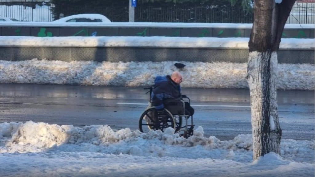 Un bărbat în scaun cu rotile străbate zăpada pe cel mai aglomerat bulevard din București